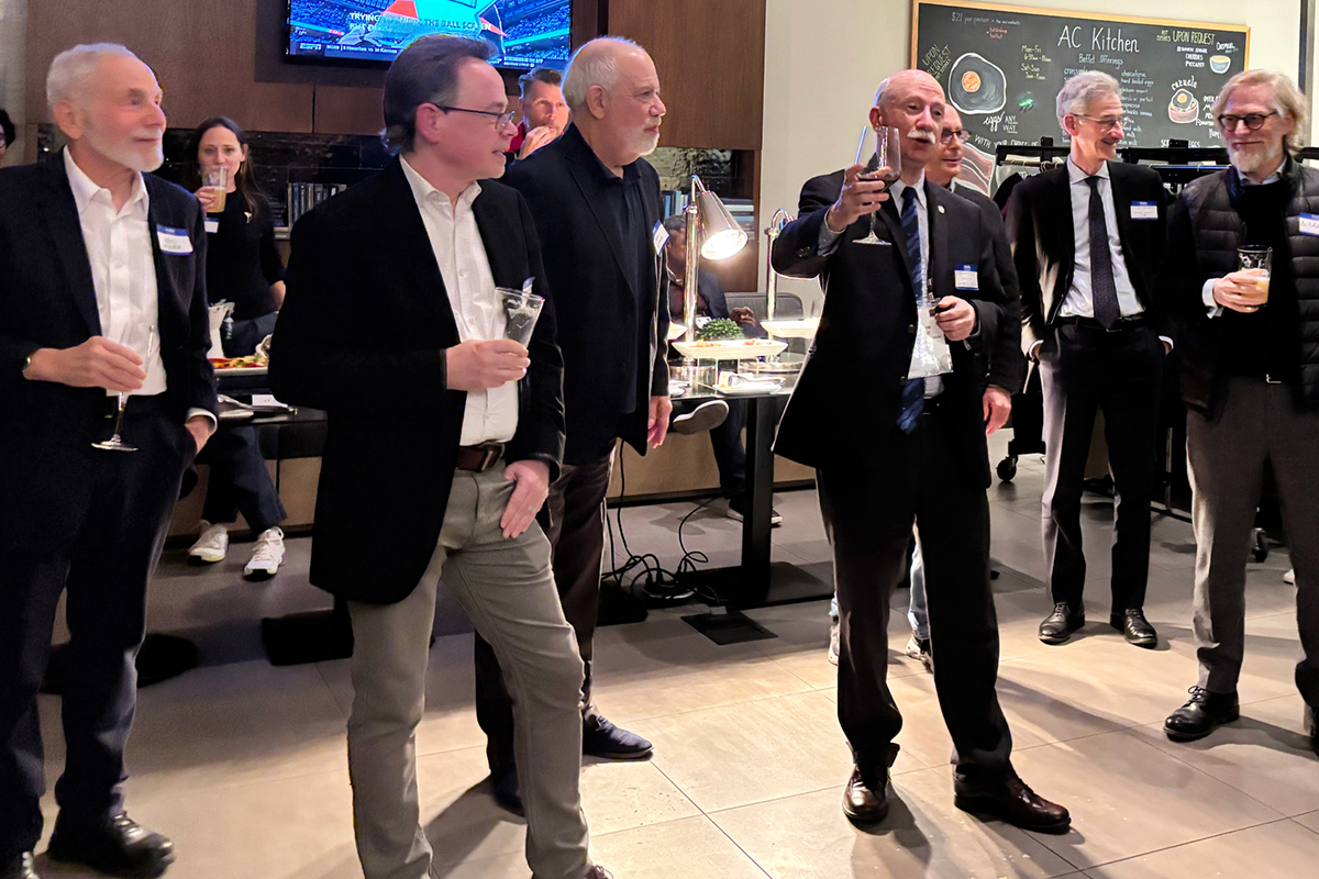 Many guests stand at an evening reception and toast their colleague, who is being honored for a lifetime of achievement.
